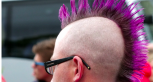 A man wearing glasses with a burgundy and hot pink mohawk hairstyle.